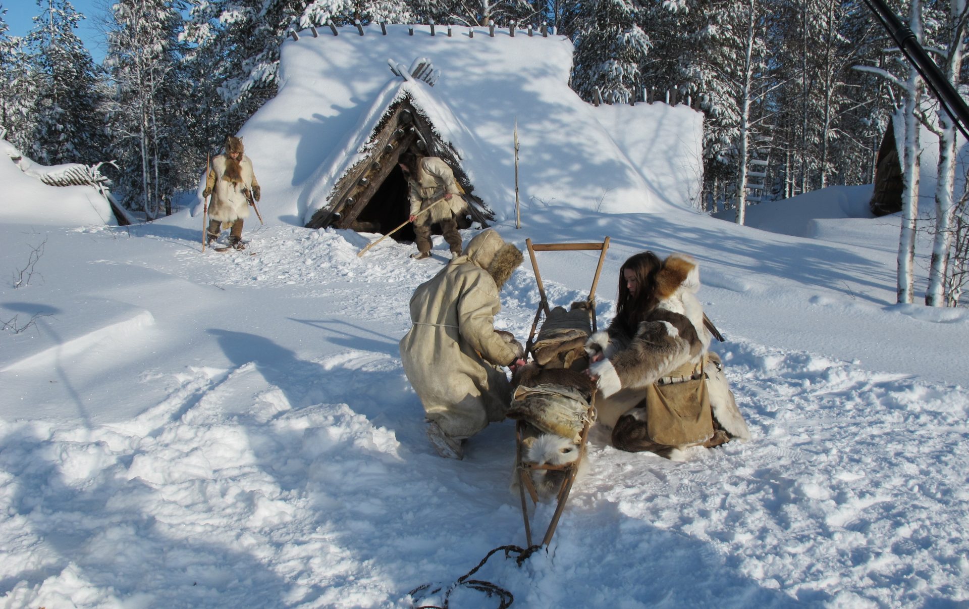 Nahkapukuihin pukeutuneita henkilöitä kivikauden kylässä arkisissa askareissa talvella.