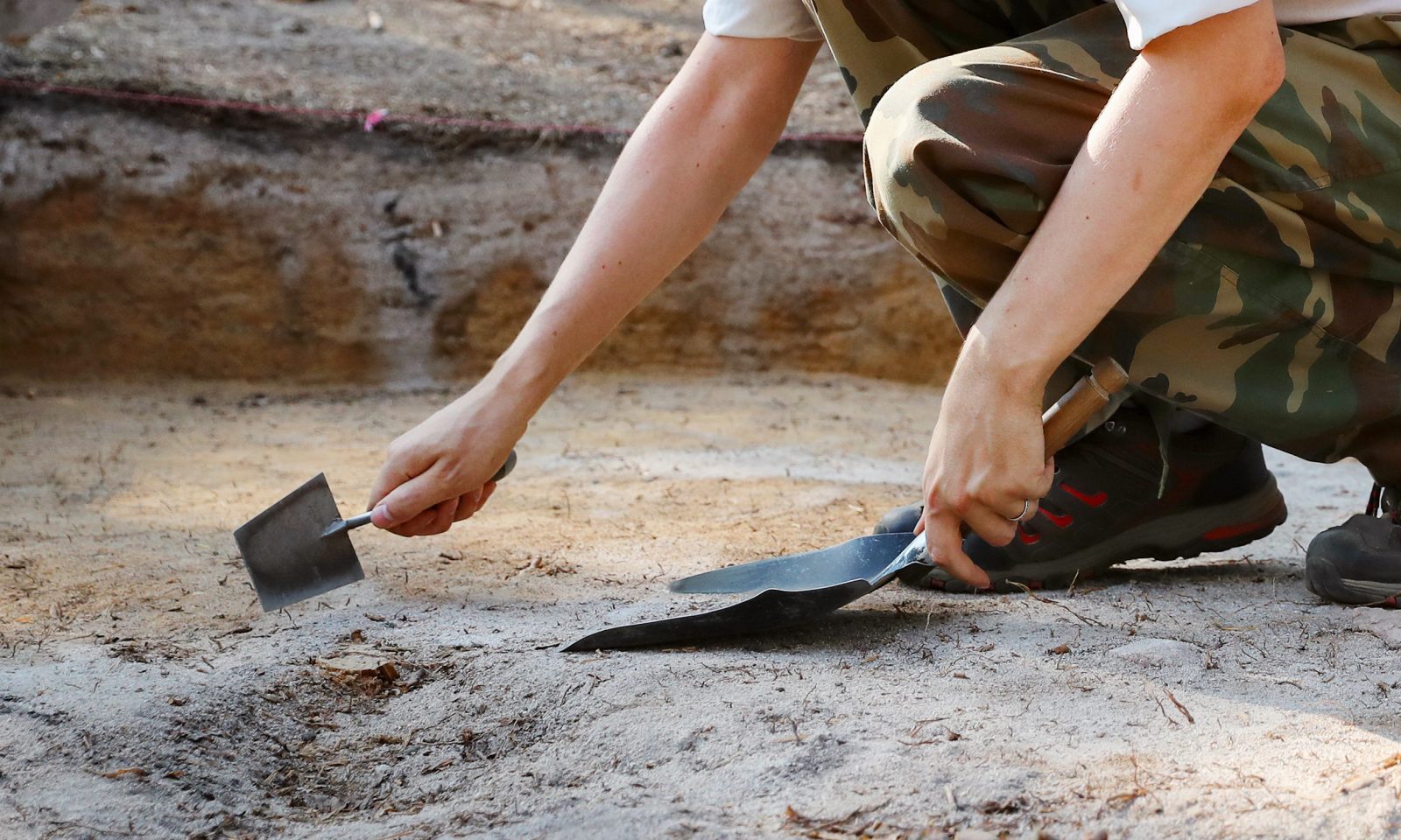 A researcher at excavations, holding a trowel and a small shovel. Close-up.