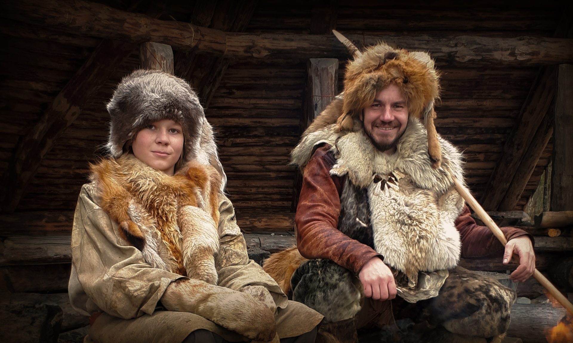 A man and a boy dressed in Stone Age costumes are sitting outside by an open roof.