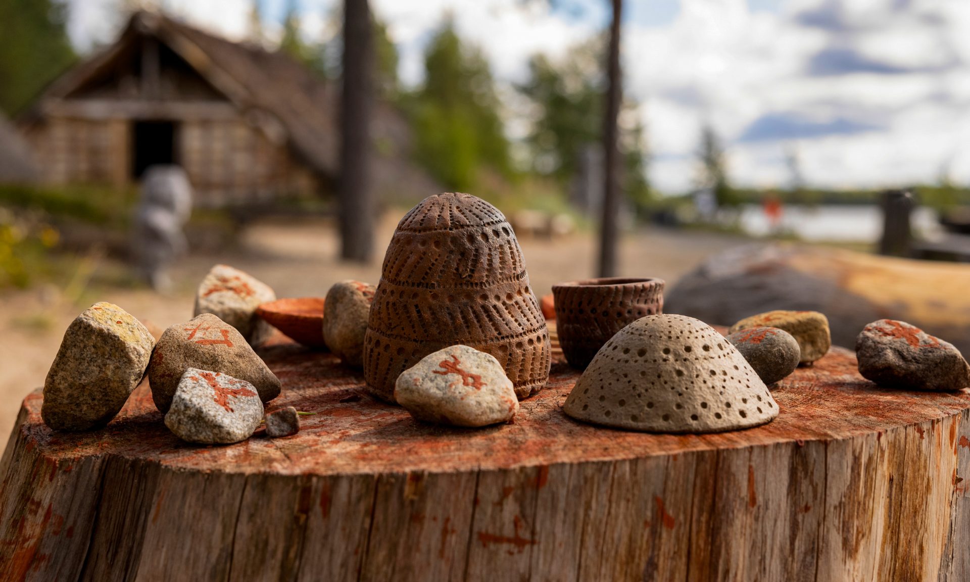 Stones and pottery objects arranged on a large stump in a Stone Age village. Patterns have been painted on the stones with red mud paint.