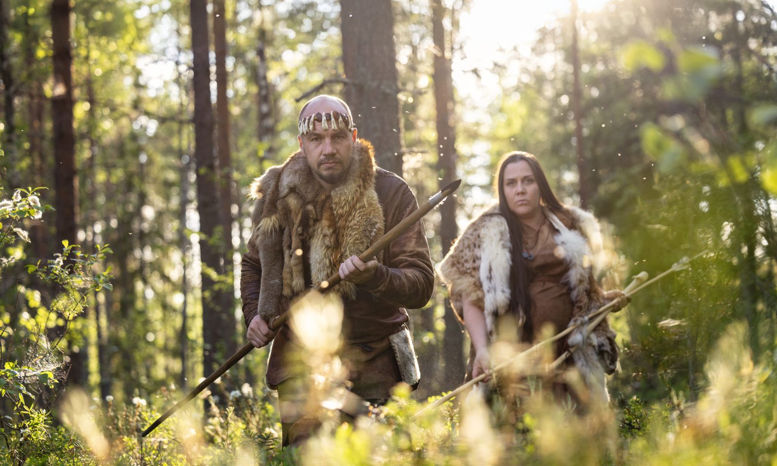Two people dressed in Stone Age leather clothing were sneaking through the forest with spears in their hands.