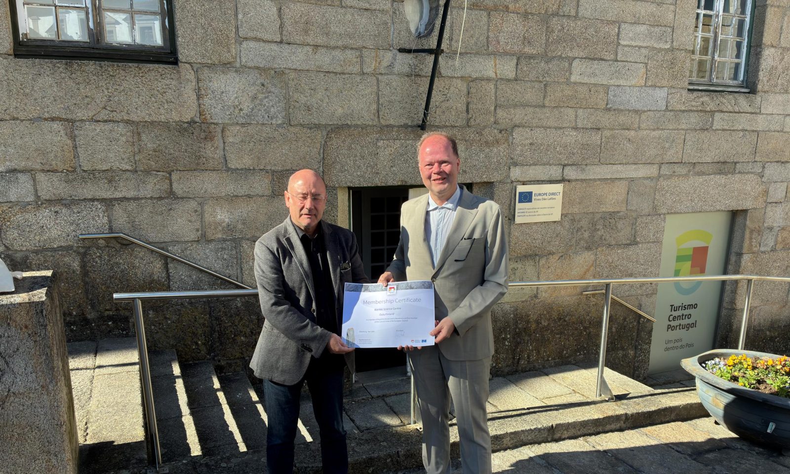 Kaksi miestä harmaissa puvuissa pitelevät yhdessä todistusta.